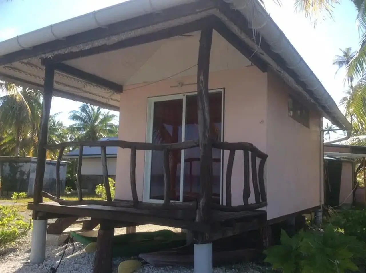 Bungalow rose à toit de tôle bleue, terrasse à rambarde de bois flotté